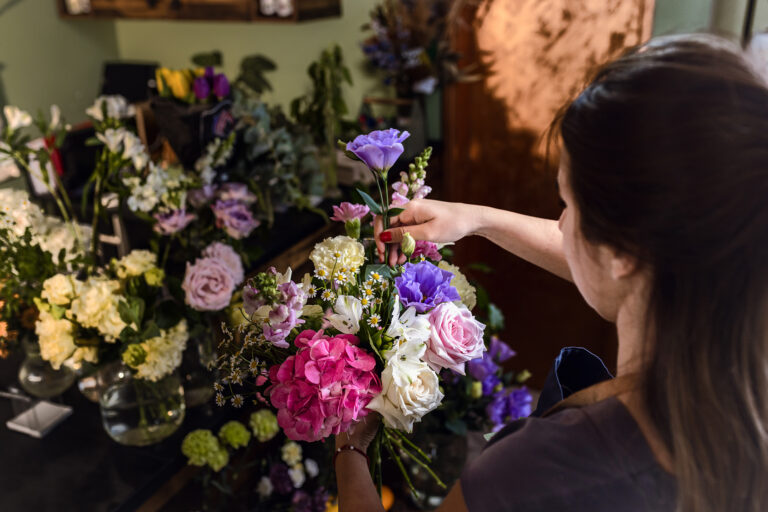 Young Woman Working In Her Flower Shop Making Bouquet With Vario